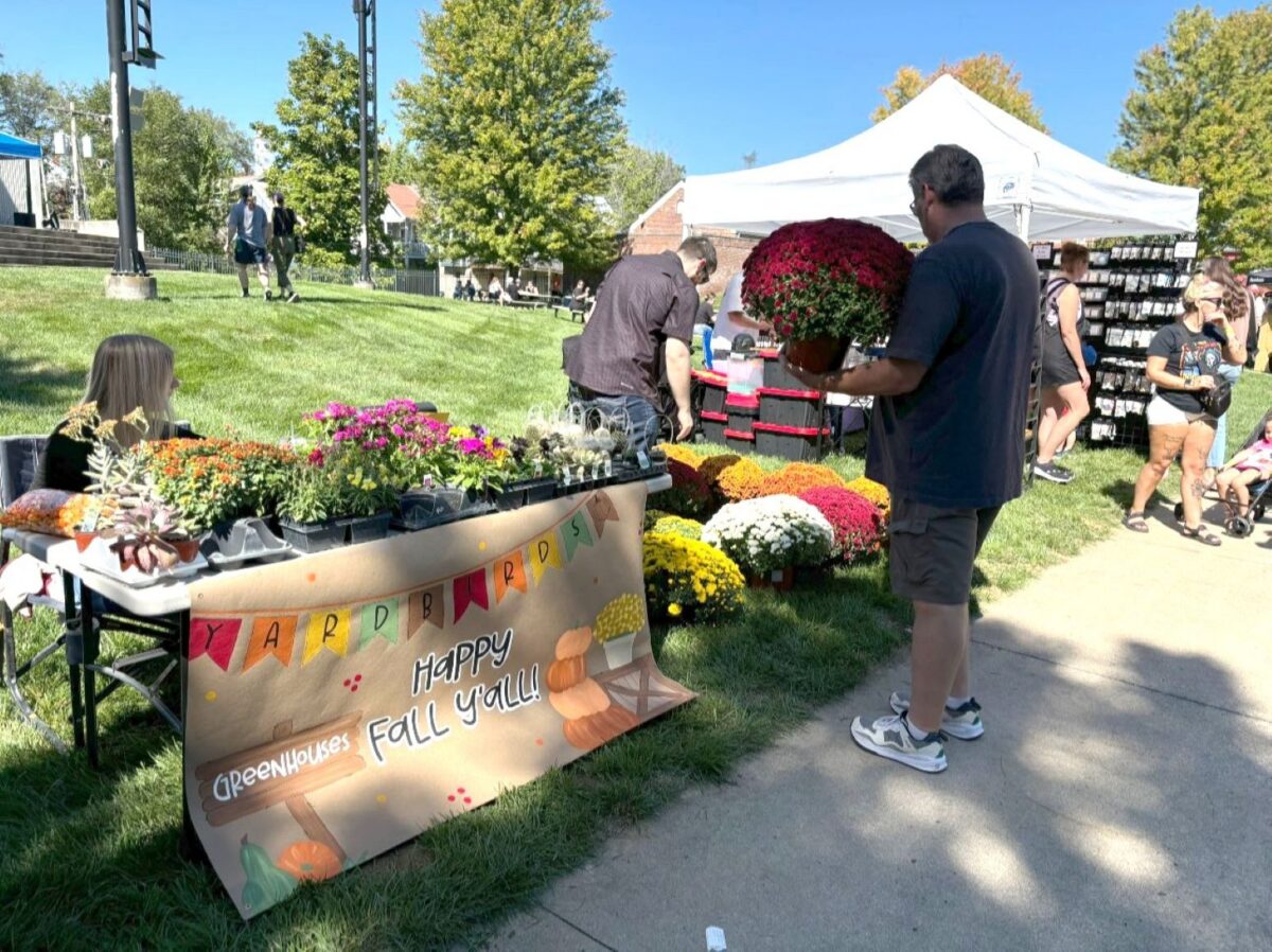 Attendees of a fall festival outside near a flower stand.