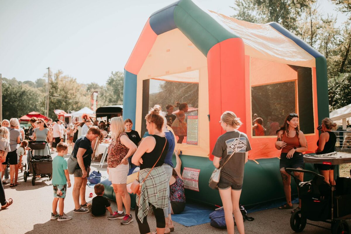 Attendees of a fall festival outside around a bouncehouse.