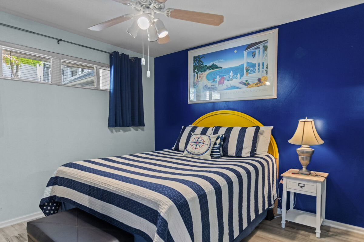 A bed with white and blue striped furnishings in the bedroom of a condo.