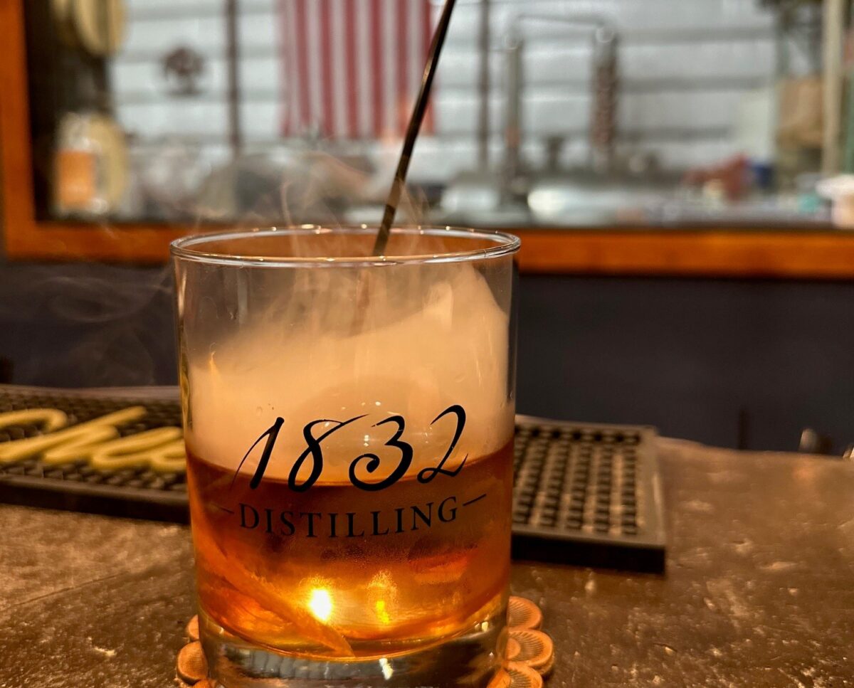 A whisky glass with liquid and smoke on a bar top.
