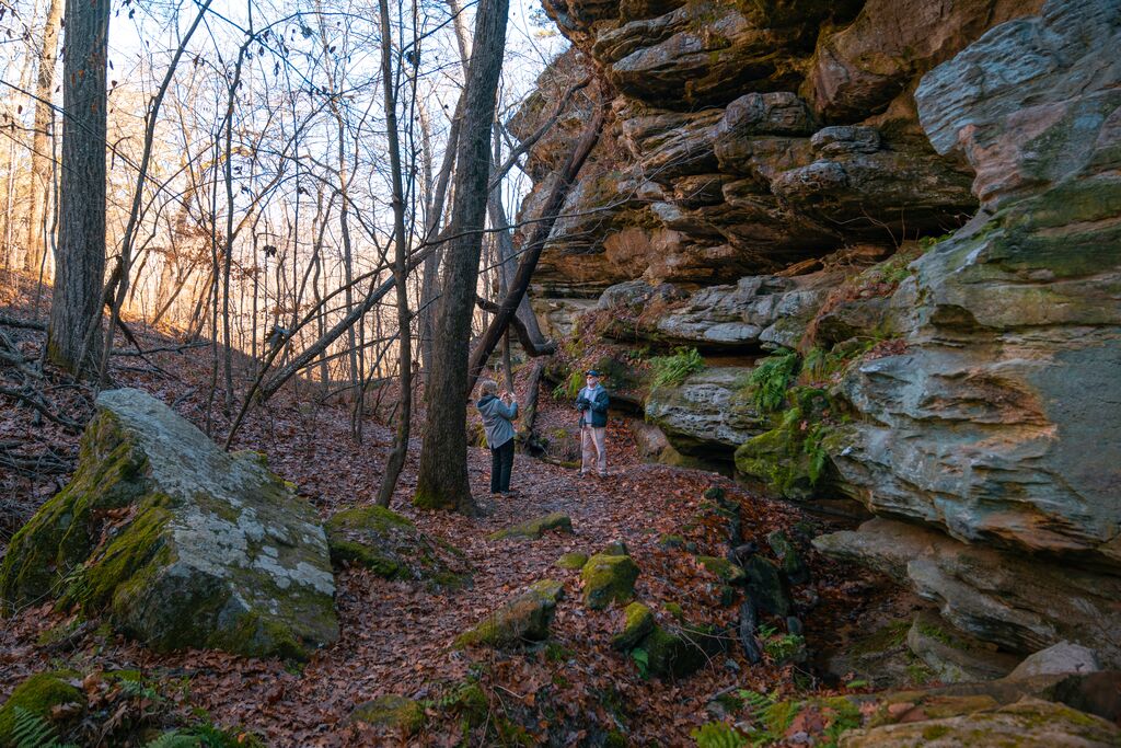 Two people stop to take a photo along a rock bluff on a trail during late fall.