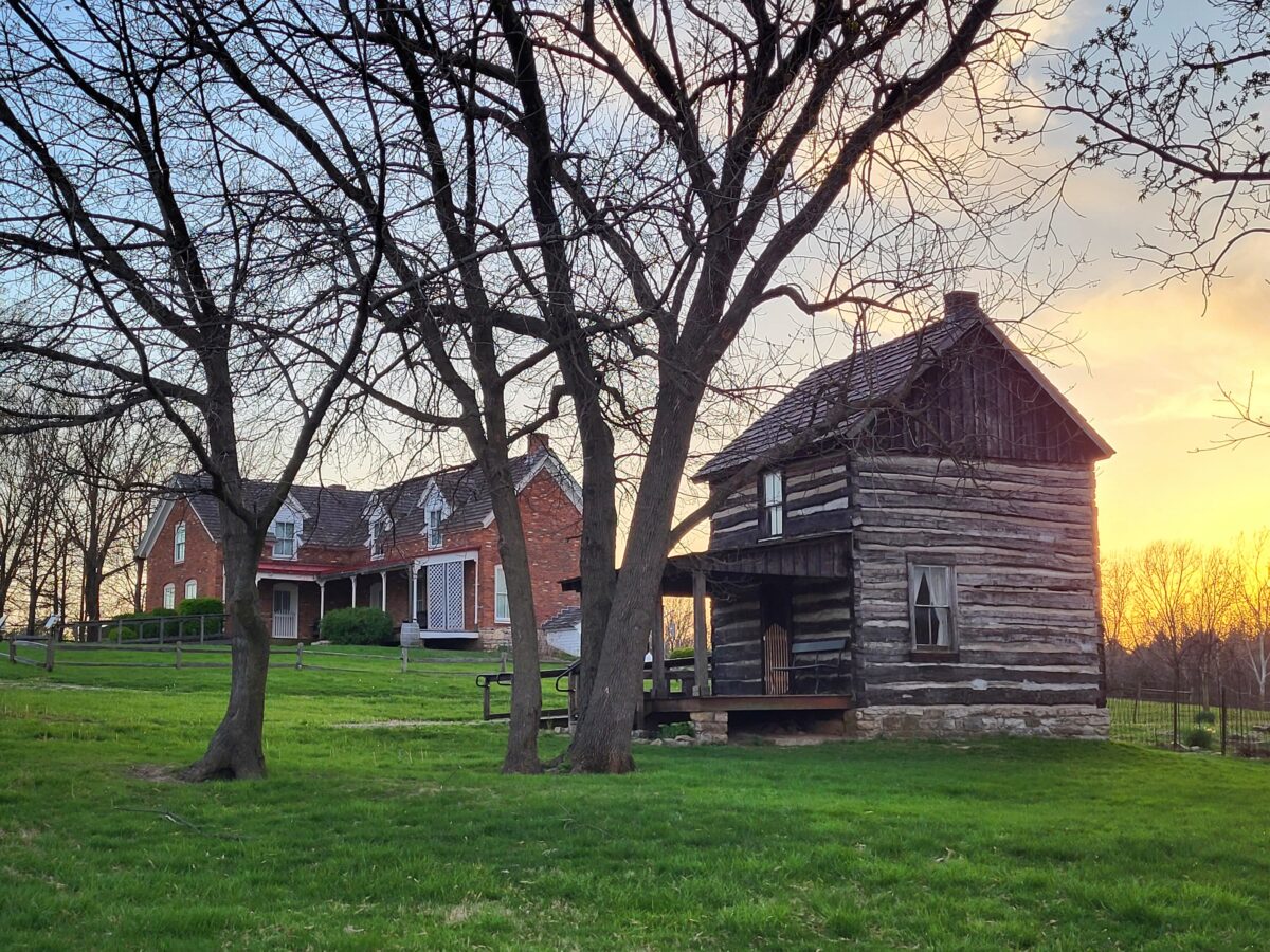 A cabin and another structure near trees and bright green grass.