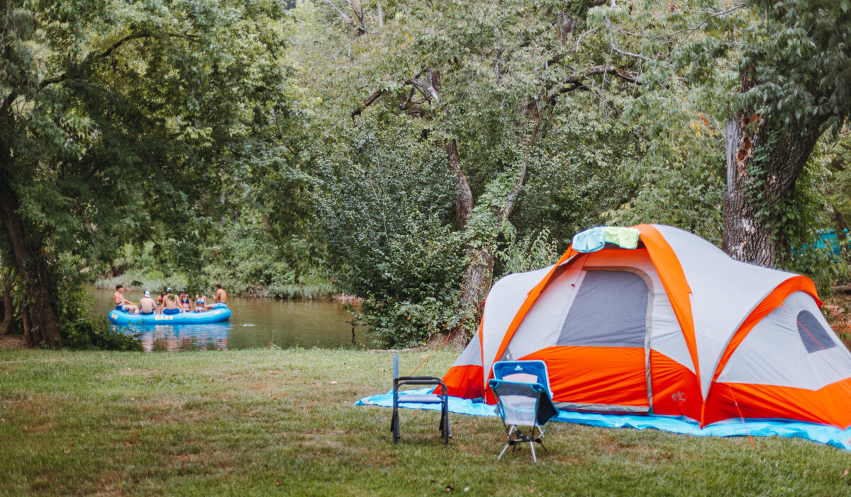 Orange and white tent in the foreground, with people boating on the river in the background.
