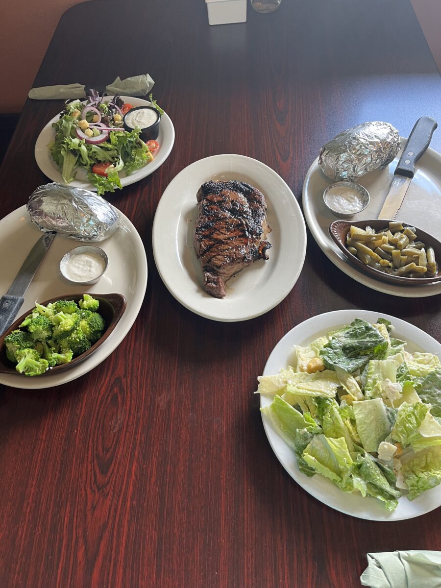 Steak plated in the middle of a table surrounded by salad and other dishes.