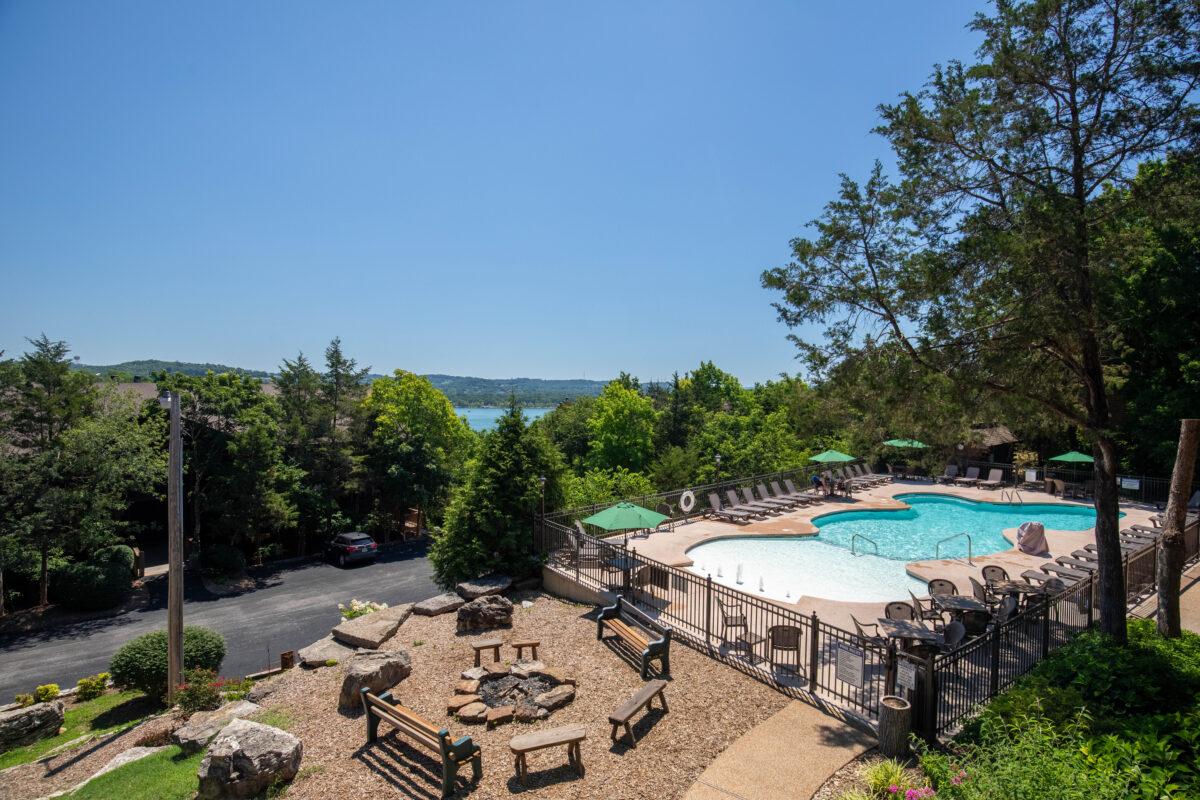 Outdoor pool and seating amid trees and a lake in the distance.
