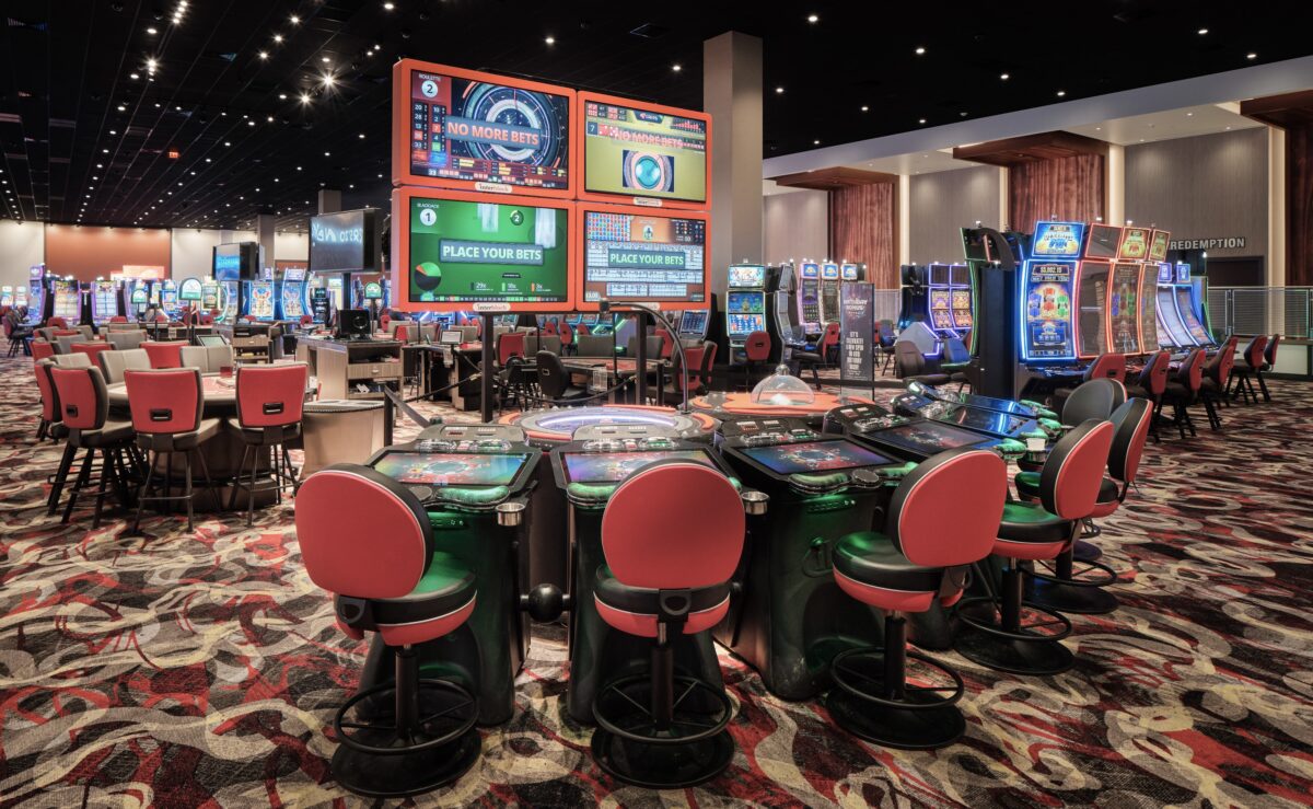 The casino gaming floor has an array of slot machines lining the floor. Table games are scattered throughout the open space.
