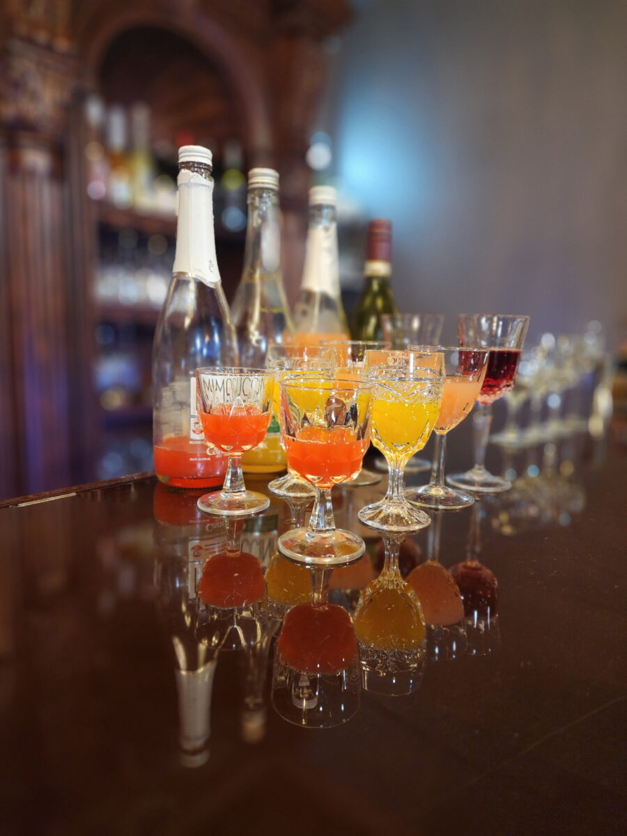 A wine flight of glasses in front of bottles on a bartop.