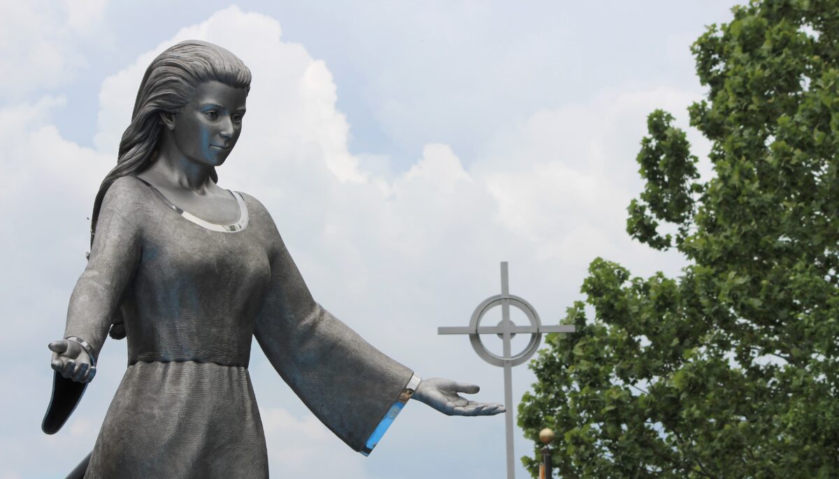 A silver sculpture of Mary with a cross in the background.