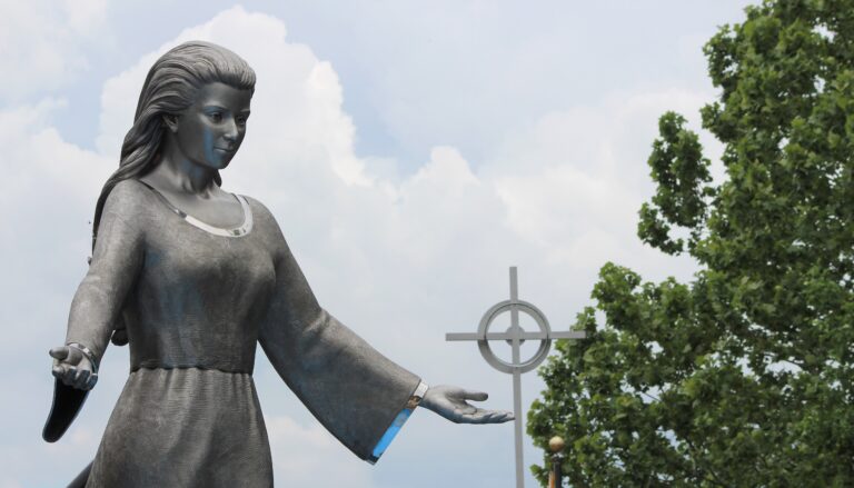 A silver sculpture of Mary with a cross in the background.