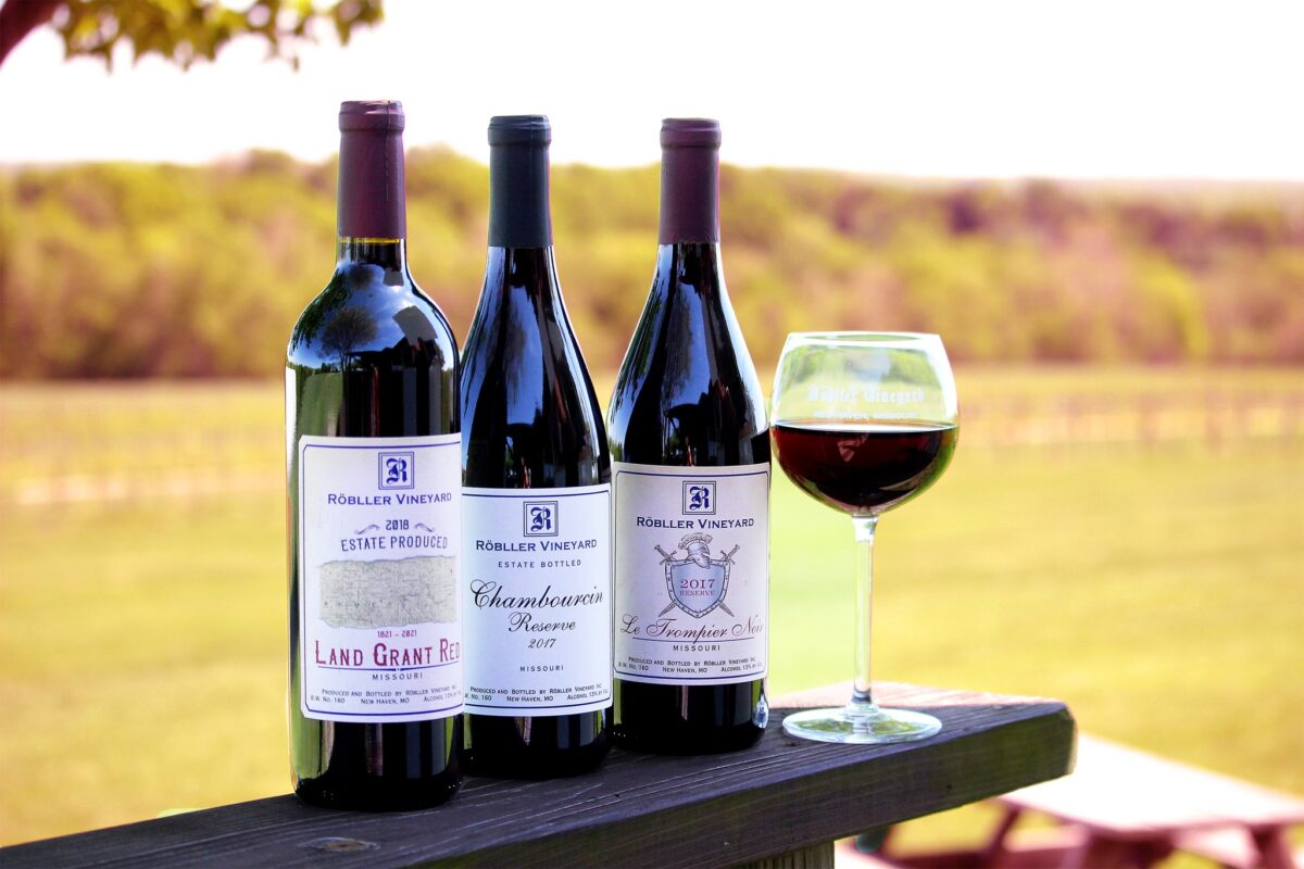 Three wine bottles and a glass on a wooden surface outdoors.