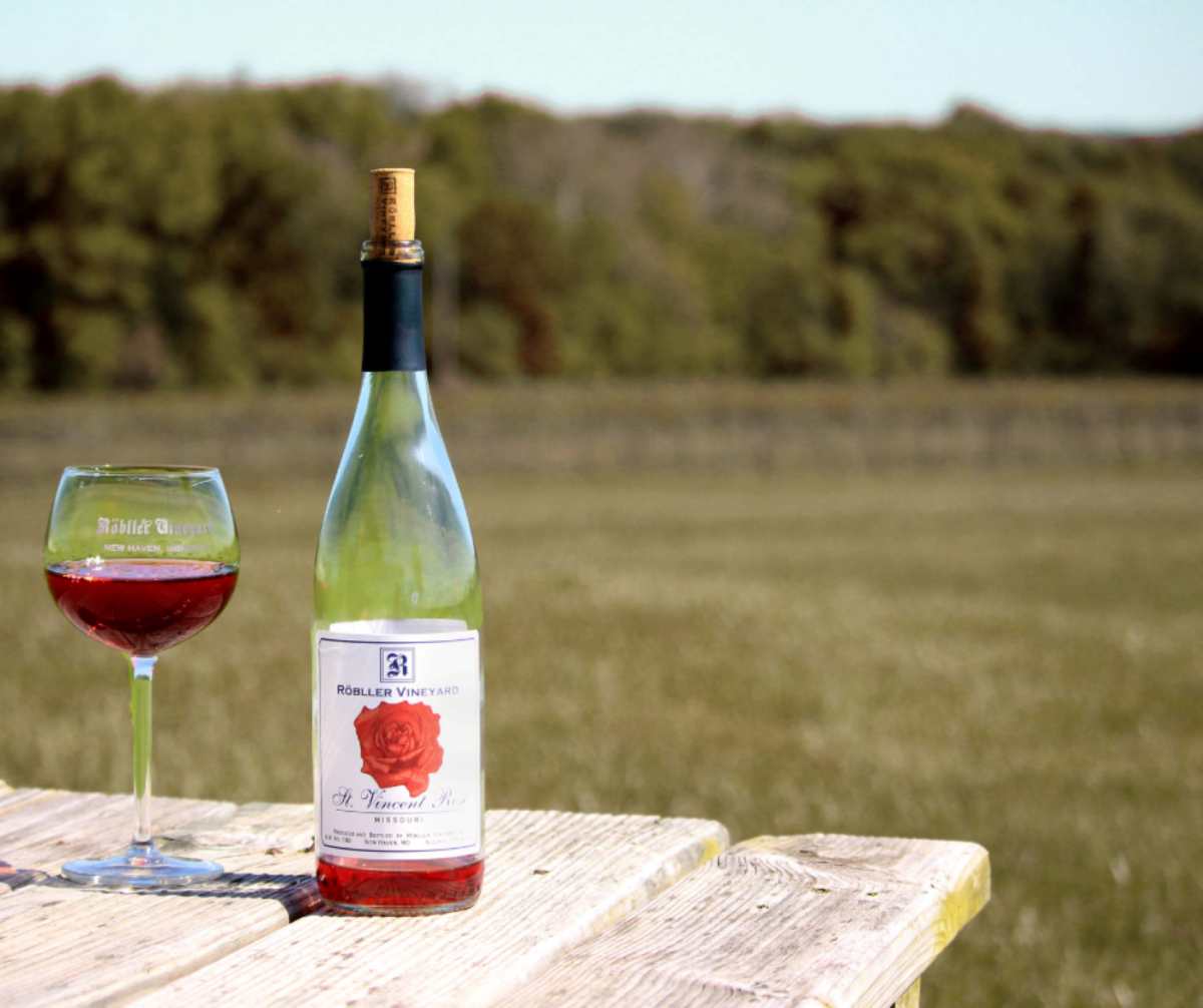 A glass of wine and a wine bottle on a table outdoors.