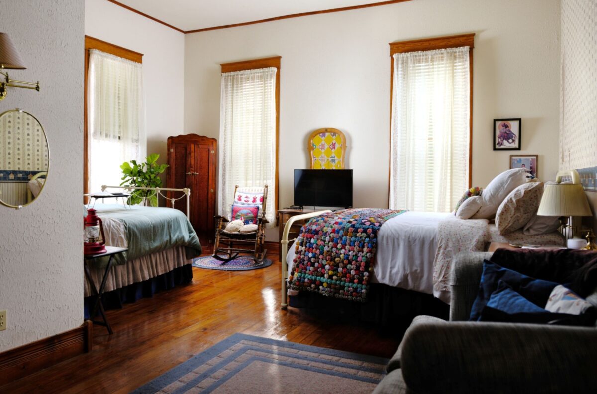A spacious room featuring queen and full size beds, an antique wardrobe, and love seat.