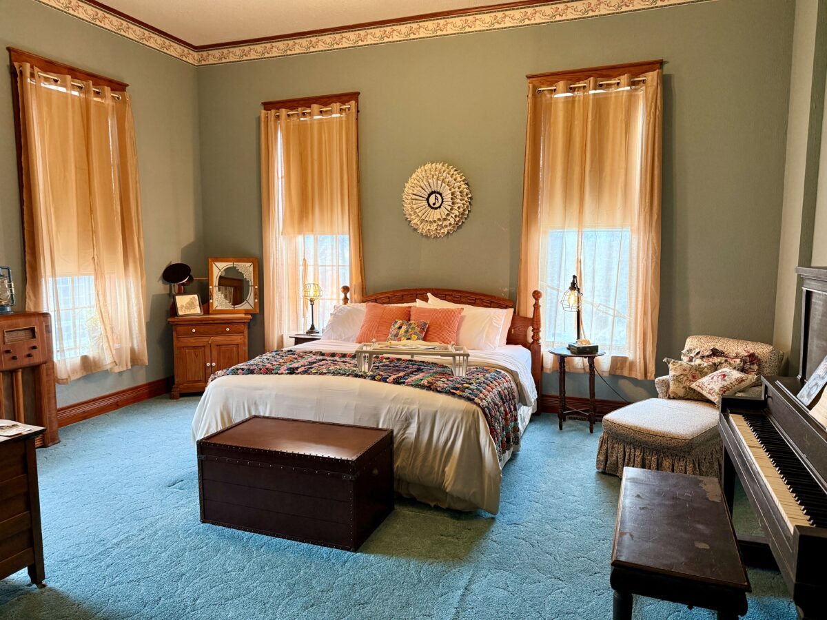 Spacious room with a king-sized bed, chaise lounge, upright piano, old time radio, and trunk.
