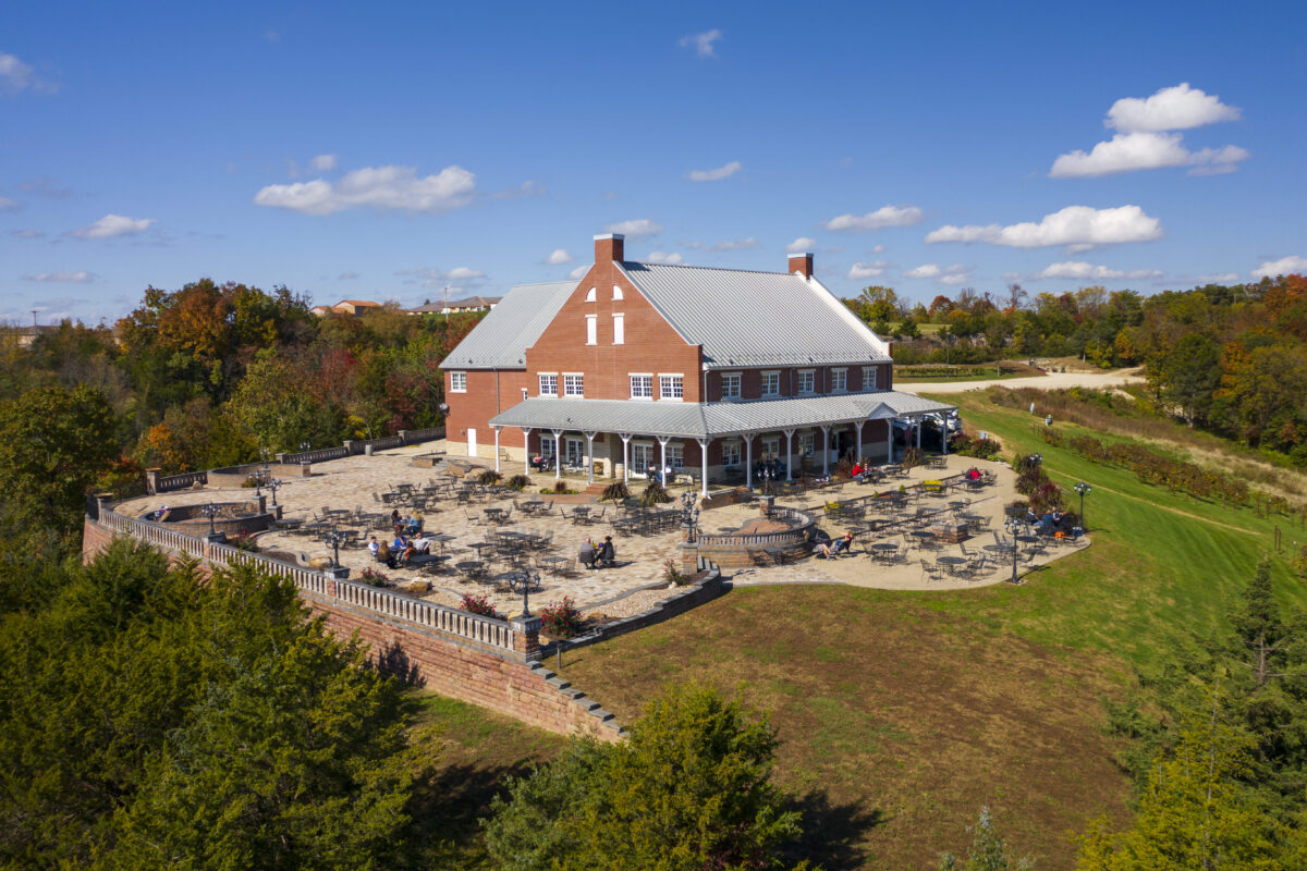 An aerial view of the Canterbury Hill Winery shows a reddish building on the top of a hill with blue skies and trees in the background
