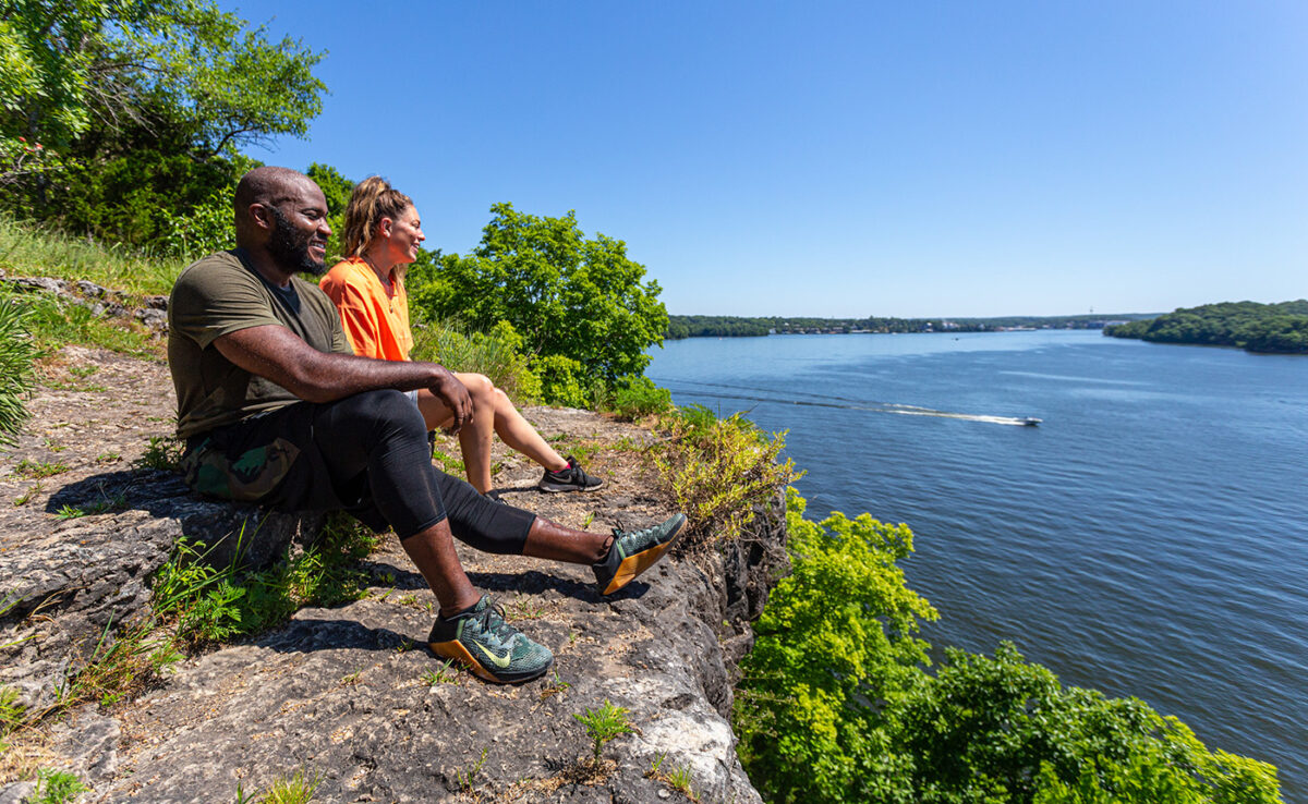A couple sits on a cliff overlooking the blue waters of Lake of the Ozarks State Park.