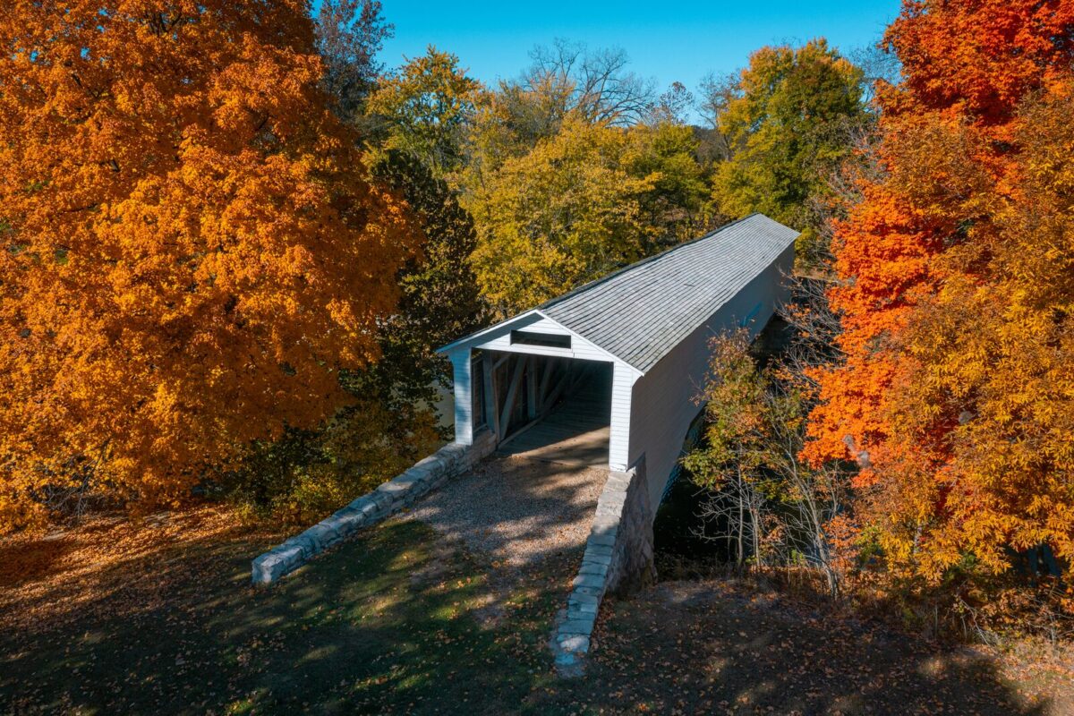A bright white covered bridge sits nestled between bright fall foliage of orange and yellow.