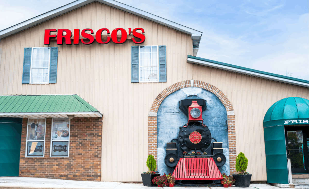 Exterior of Frisco’s Grill & Pub, a tan and brick building in Cuba, Missouri, with bright red signage and a large decorative train engine mural built into the front facade, symbolizing the town’s railroad heritage.