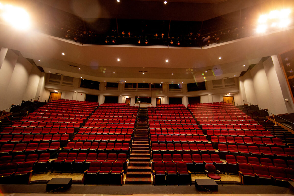 Stage view of audience. Rows of red chairs with center aisle.