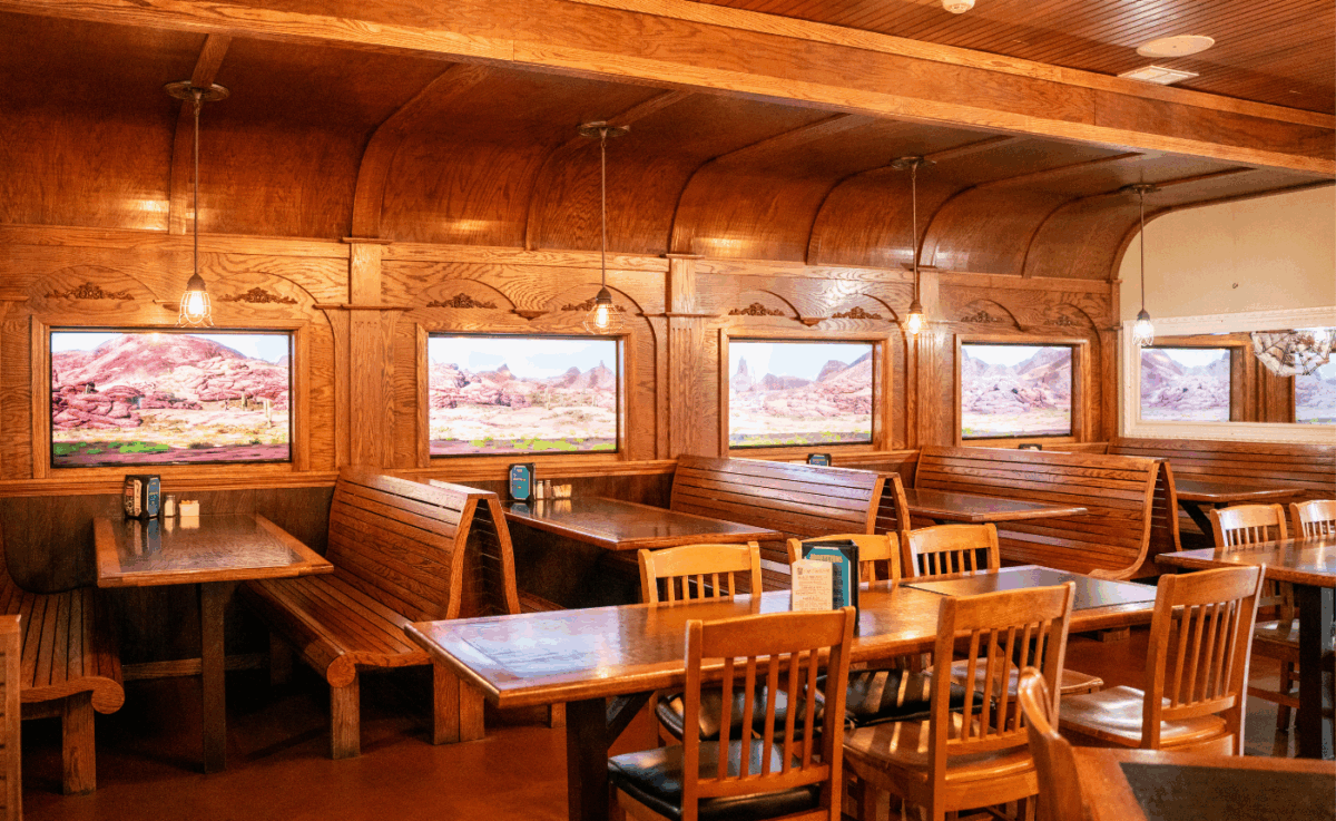 Interior of Frisco’s Grill & Pub showcasing a warm, wood-paneled dining room designed like a classic train car, with vintage lighting, booth seating, and scenic Western landscape murals in each window frame.
