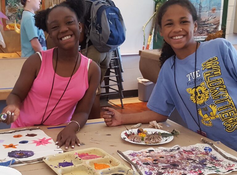 Girls smile as their artwork sits in front of them