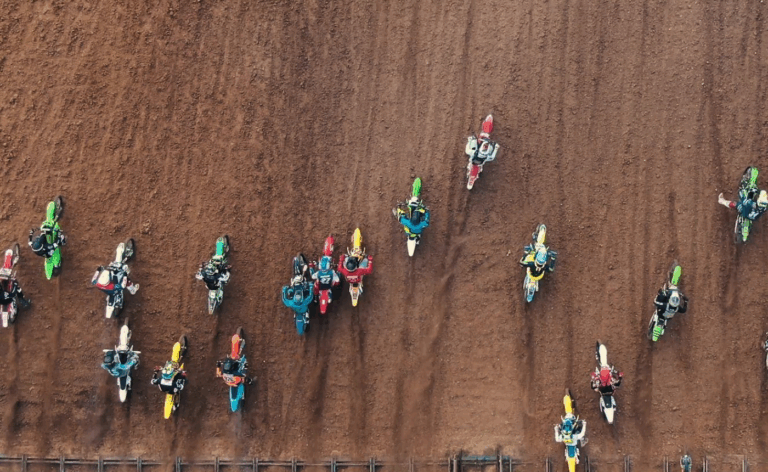 Several riders on colorful motorcross bikes ride over the dirt.