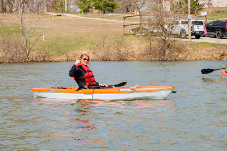 A person in an orange life jacket waves from a canoe.