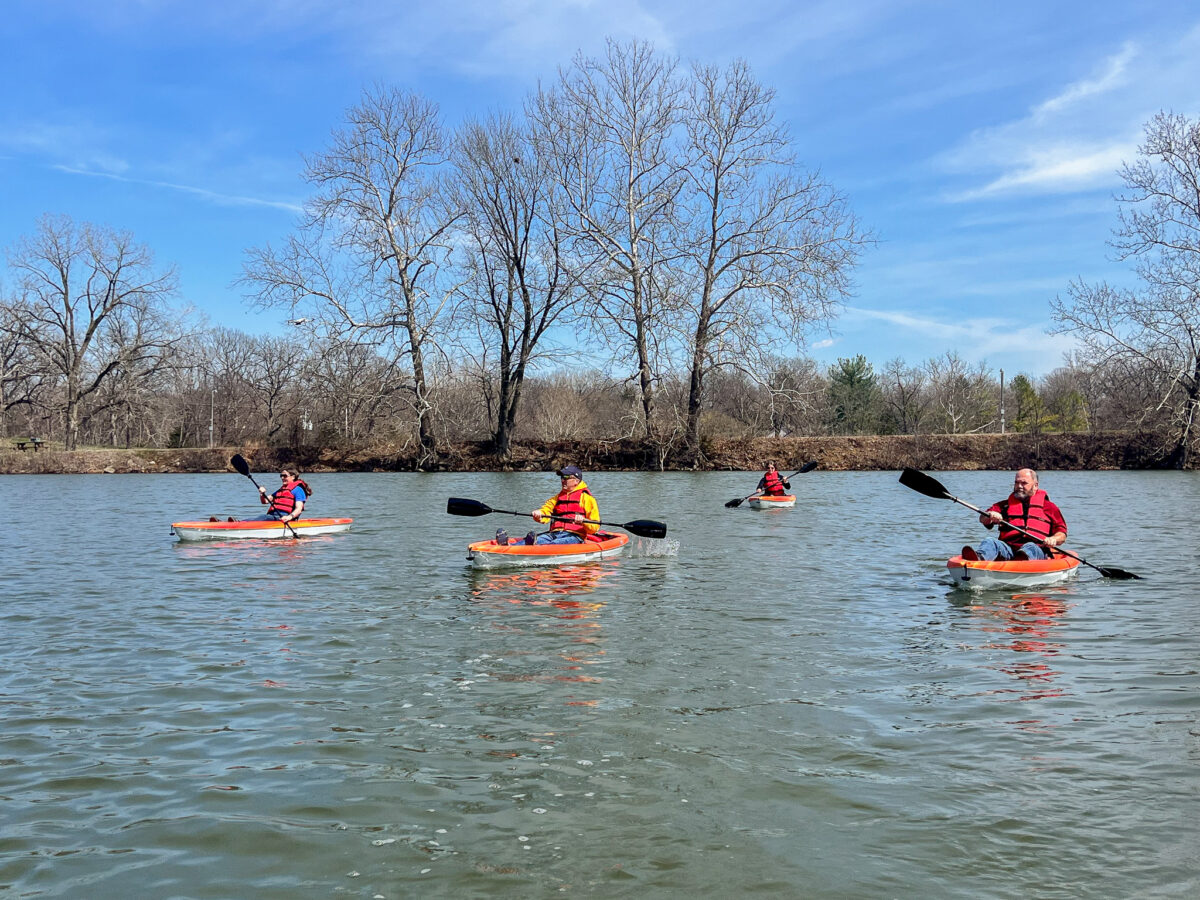 Several people in orange life jackets in kayaks on a body of water.
