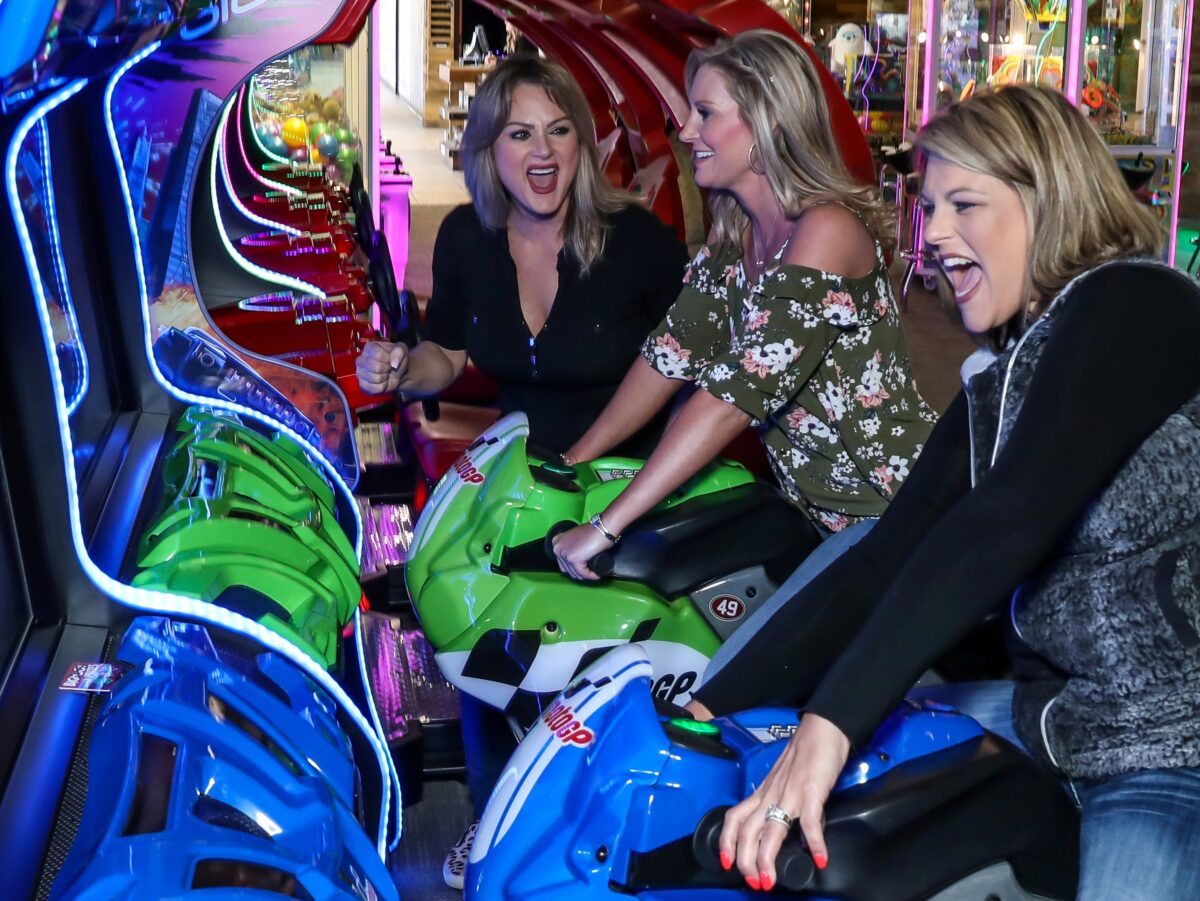 three women play and laugh in an arcade.