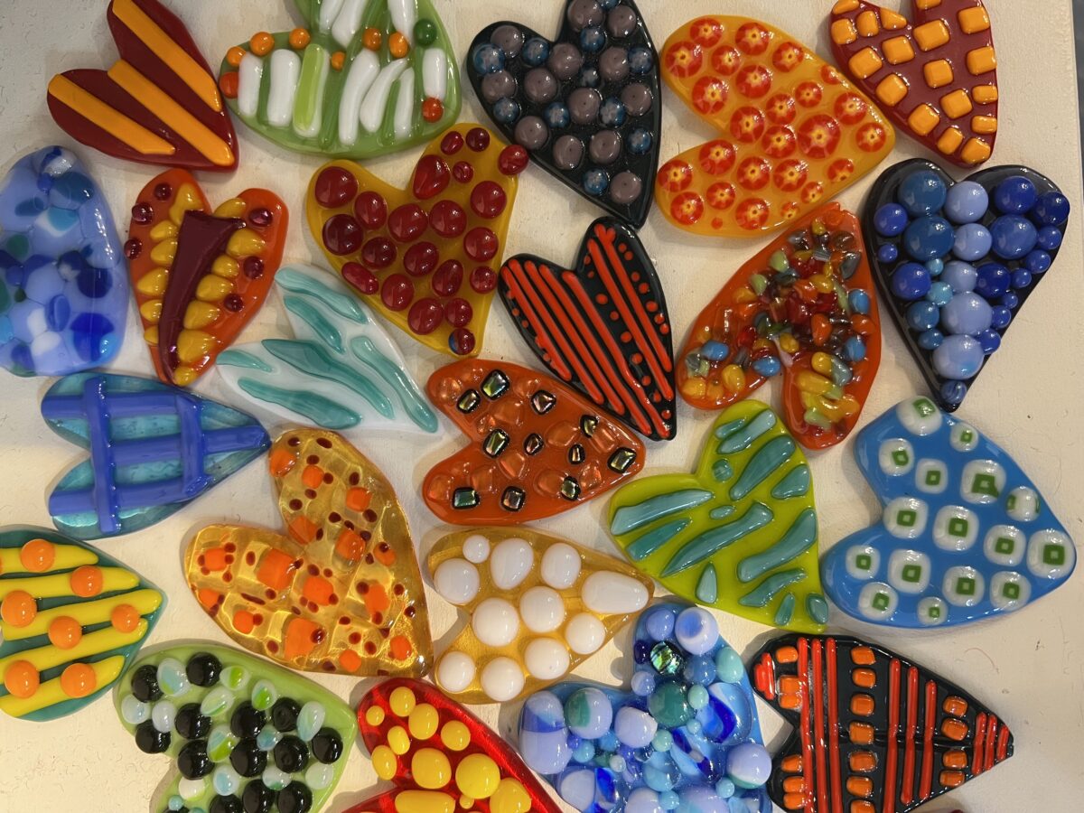Colorful, intricate heart-shaped items arranged on an off-white surface.