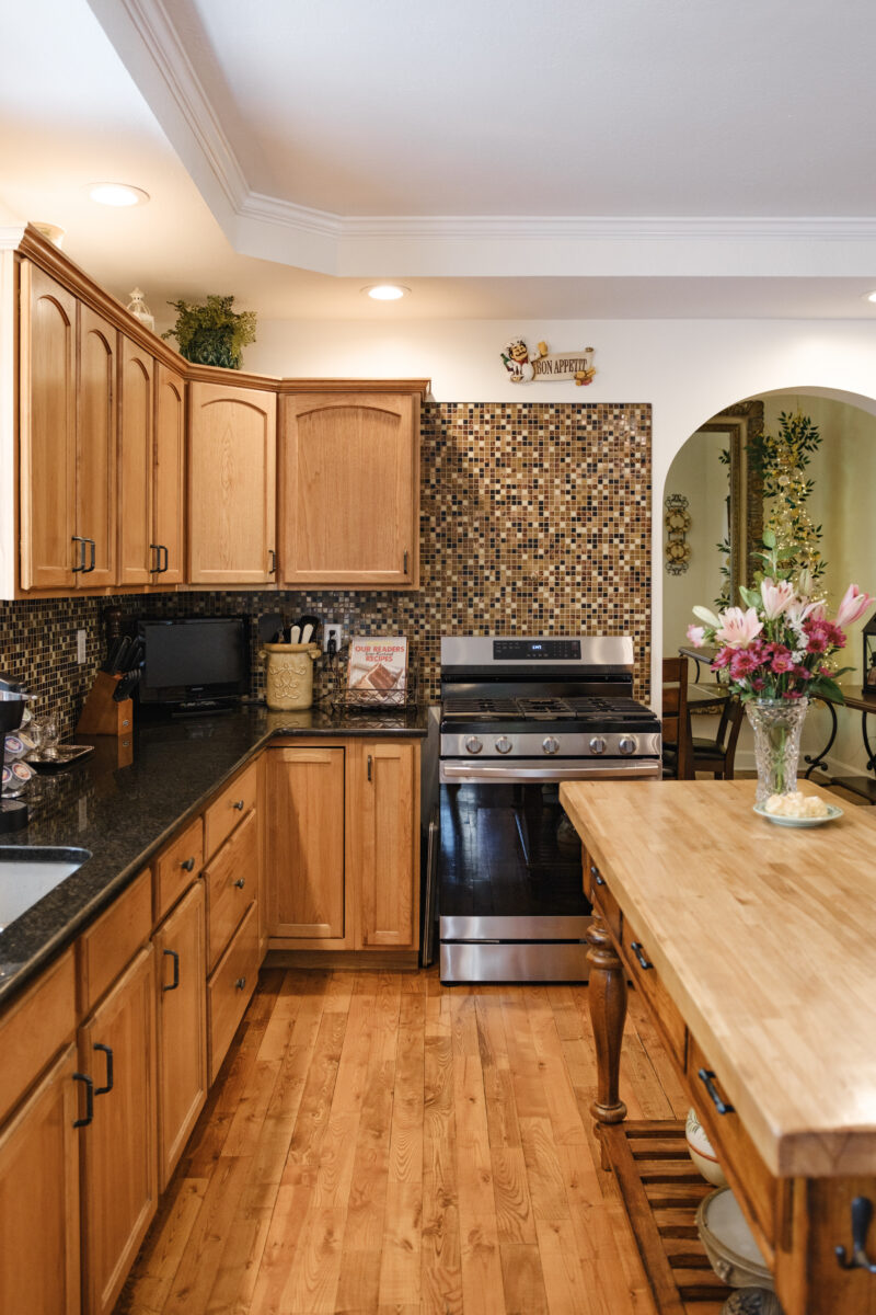 Warm-toned kitchen with wooden cabinets, stainless steel stove, mosaic backsplash, and island countertop.