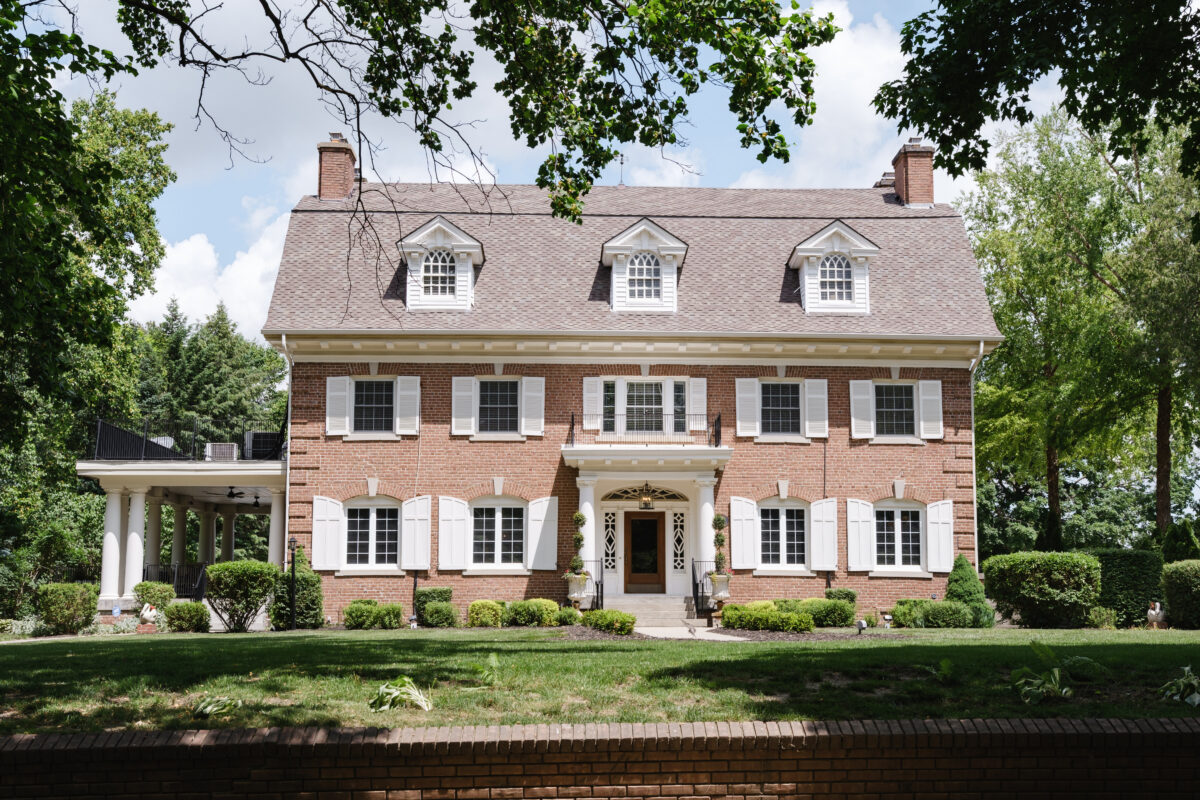 Large brick home with white shutters, symmetrical windows, and landscaped front yard.