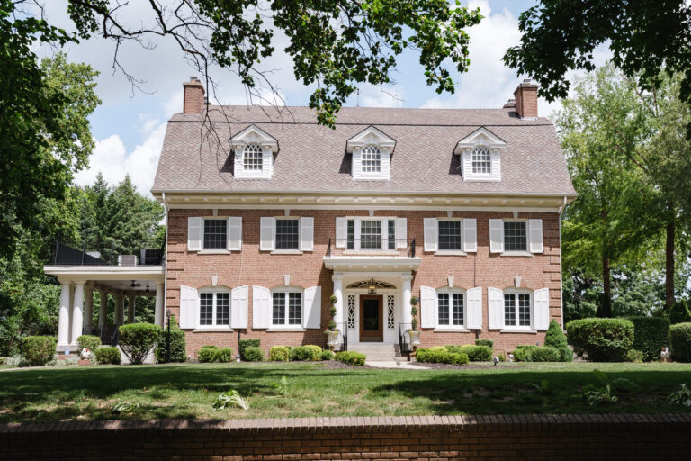 Large brick home with white shutters, symmetrical windows, and landscaped front yard.