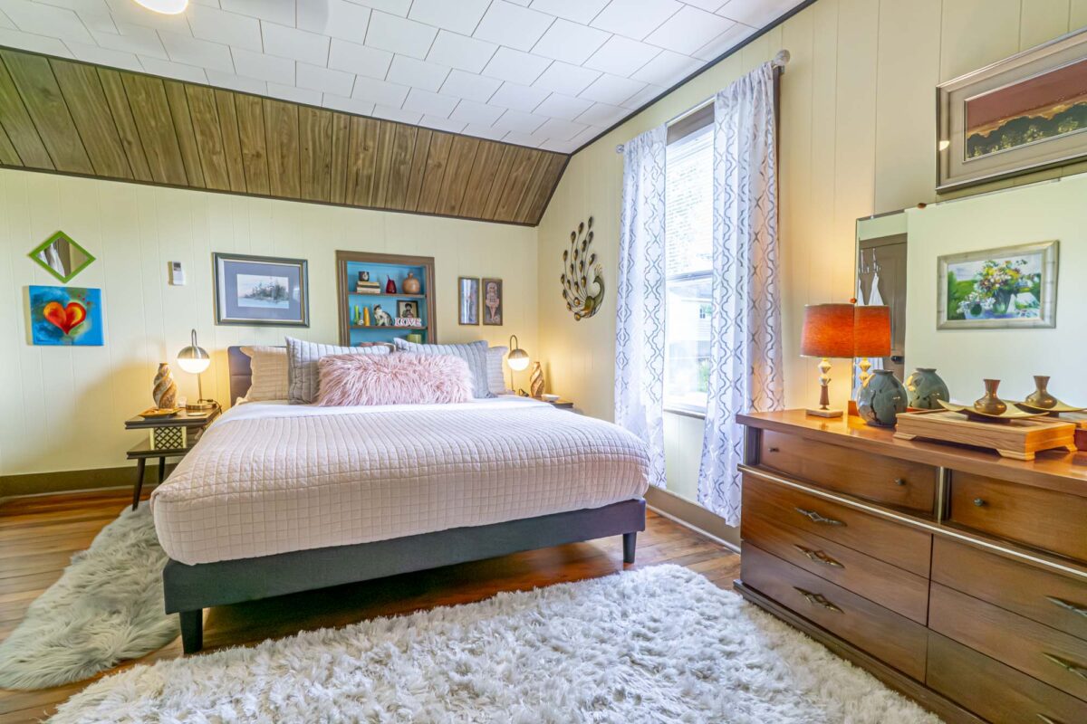 A bedroom with pink furnishings, a dresser and a vintage-style orange lamp.