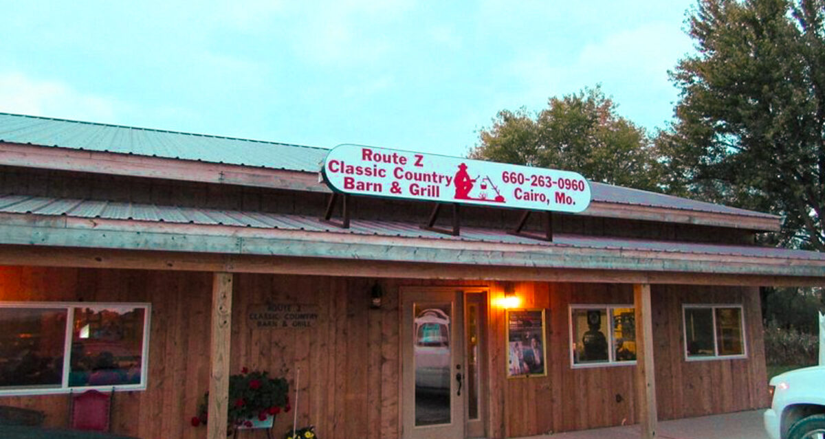 The outside of a country bar with wood aesthetics and a sign over the top.