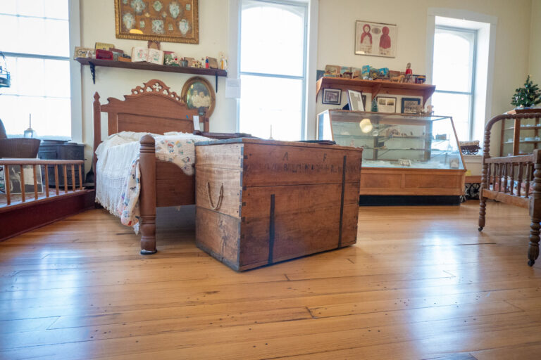 Artifacts, including a vintage bed and trunk, in a museum.