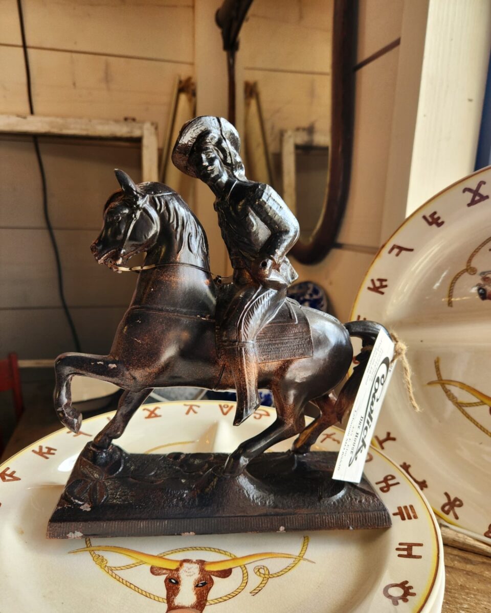 Une petite statue en bronze avec cow-boy monte un cheval au magasin d'antiquités de la maison sèche Cowlick. La statue se trouve sur un plat en verre contenant le design de vache Texas Longhorn.
