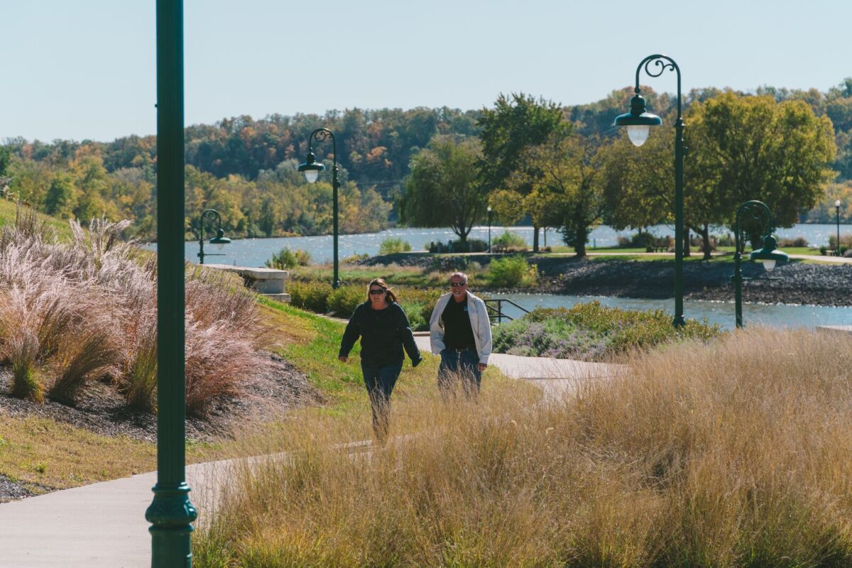 Un couple marche le long d'une rivière aligné sur le sol dans le port de Drake dans la province de Benton, Missouri, avec des feuilles d'automne colorées et de l'eau bleue calme en arrière-plan.