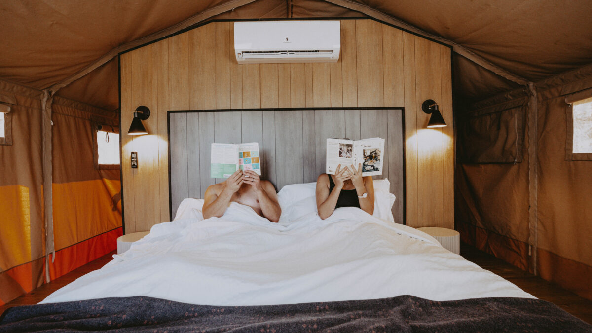 A couple sits in bed with literature in front of their faces.