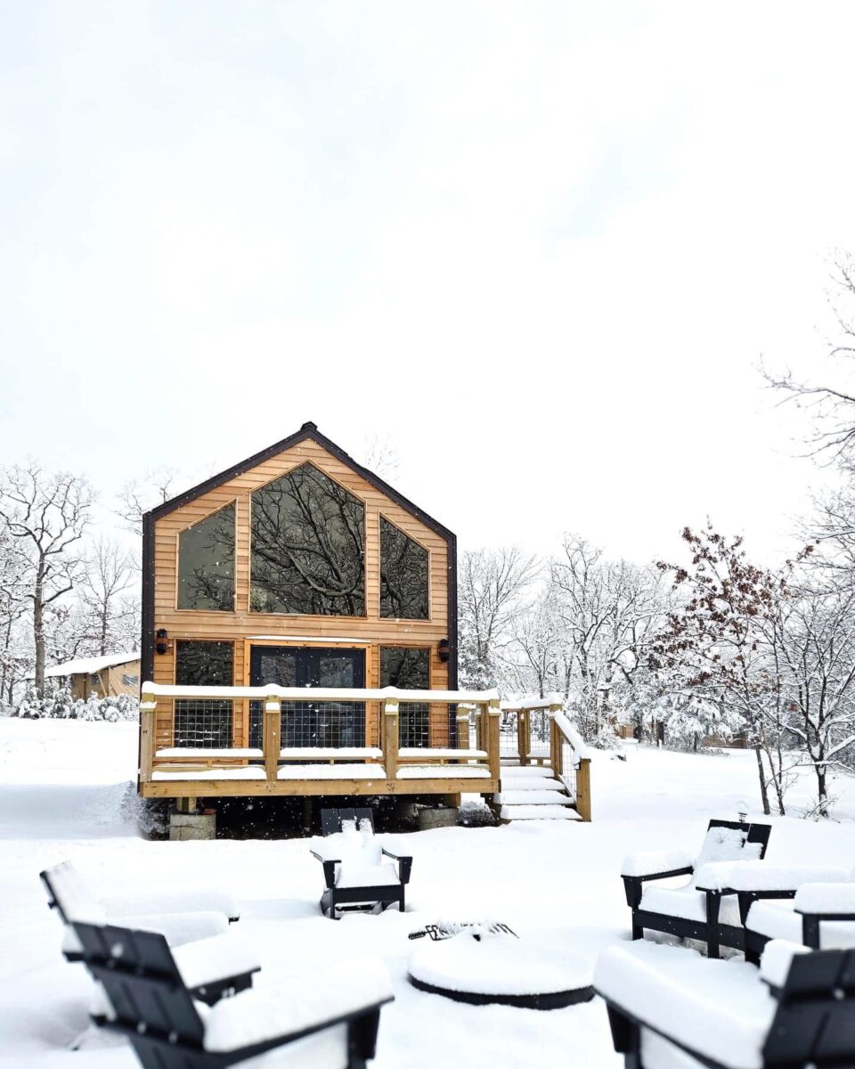 A modern log cabin with many windows sits quietly in a dusting of fresh white snow.