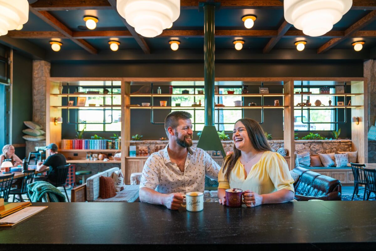A couple sits at the bar in the lobby of a hotel while drinking beverages and laughing.