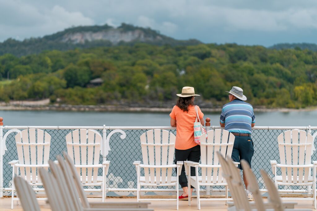 A couple stands on the deck of a boat looking out at the scenery.