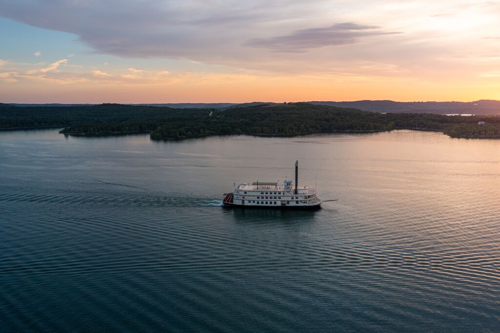 A Large paddle boat glides through the water of a lake in the Ozarks at sunset.