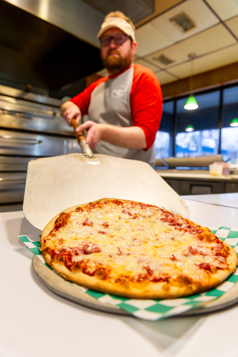 An employee shows off a freshly-made pizza on a pan at Pagliai's Pizza.