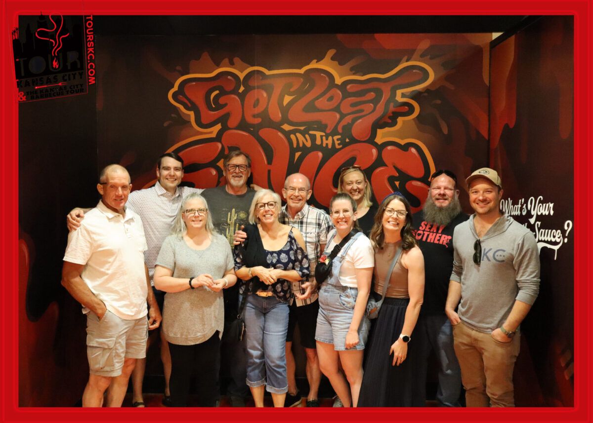A group of adults poses in front of a mural that says get lost in the sauce.