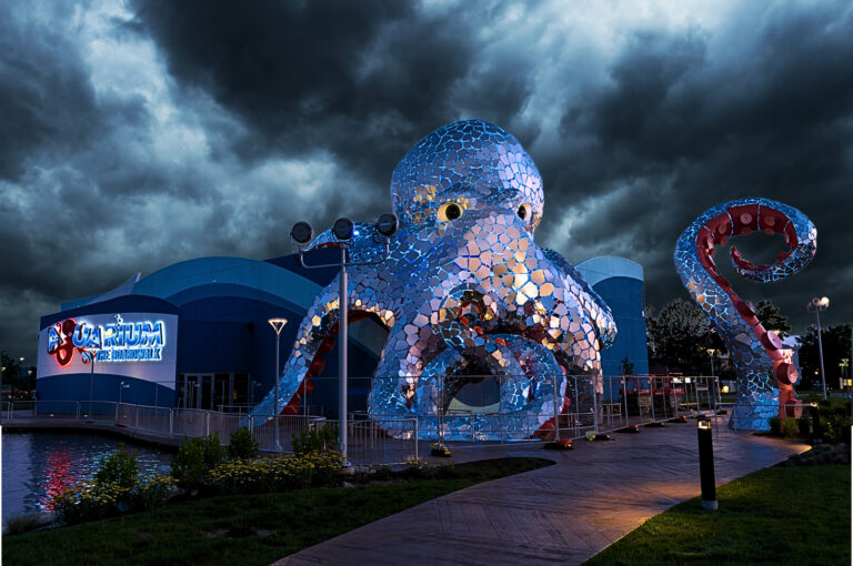 A photo of the Branson Aquarium at night, featuring a large shimmering octopus covering the building.