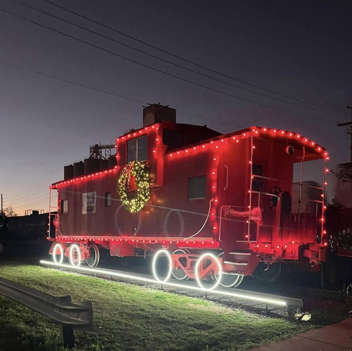 A bright red caboose lined with holiday lights photographed after dark.