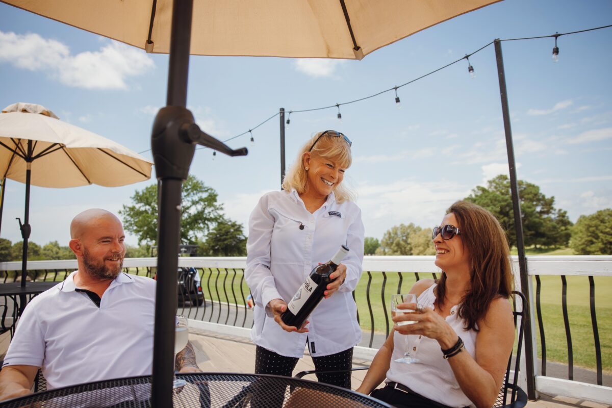 A server offers wine to two guests at an outdoor table at Hidden Trails Country Club.