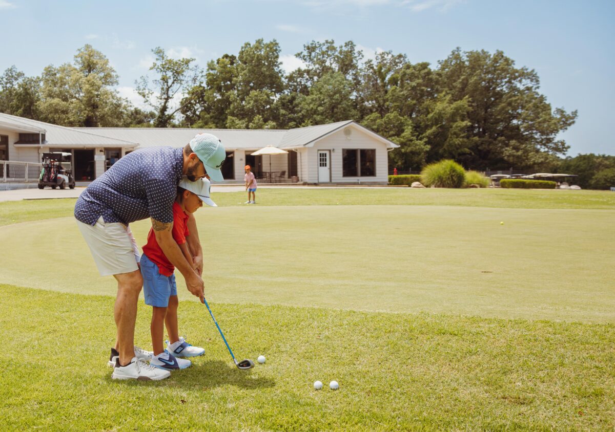 A man helps a child golf at Hidden Trails Country Club.