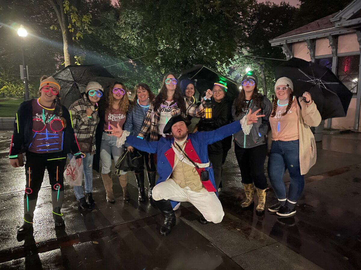 A guide in colonial dress poses with a tour group at night.
