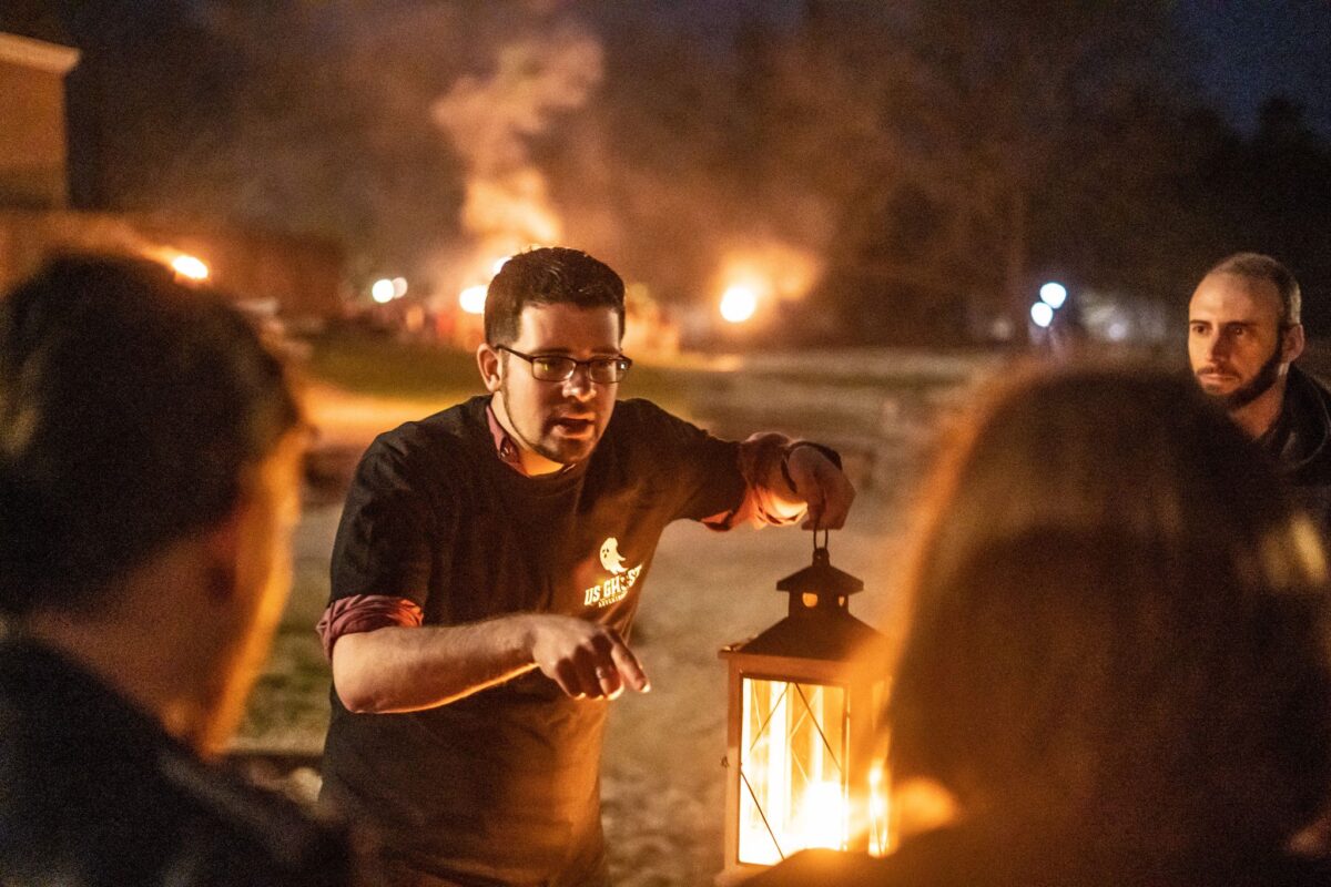 A man with a lantern talks to attendees at night.